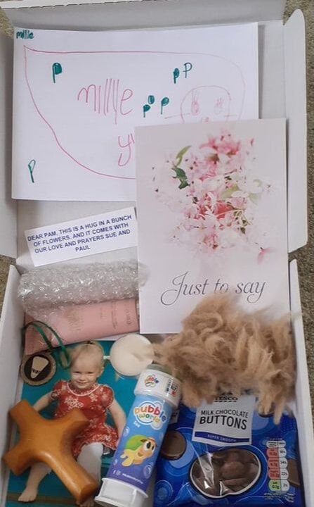 A comfort box including a child's drawing, greetings cards, bubblewrap, hand cream, a child's photo, a candle, a wooden cross, a tub of bubbles and some chocolate buttons