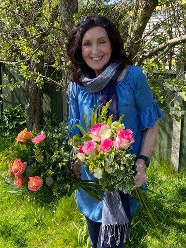 Picture in a garden of volunteer Kate smiling and holding handmade flower bouquets
